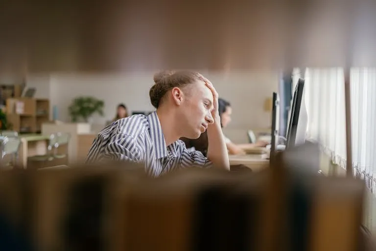 A student appears stressed while studying in a library, focusing on a computer screen.